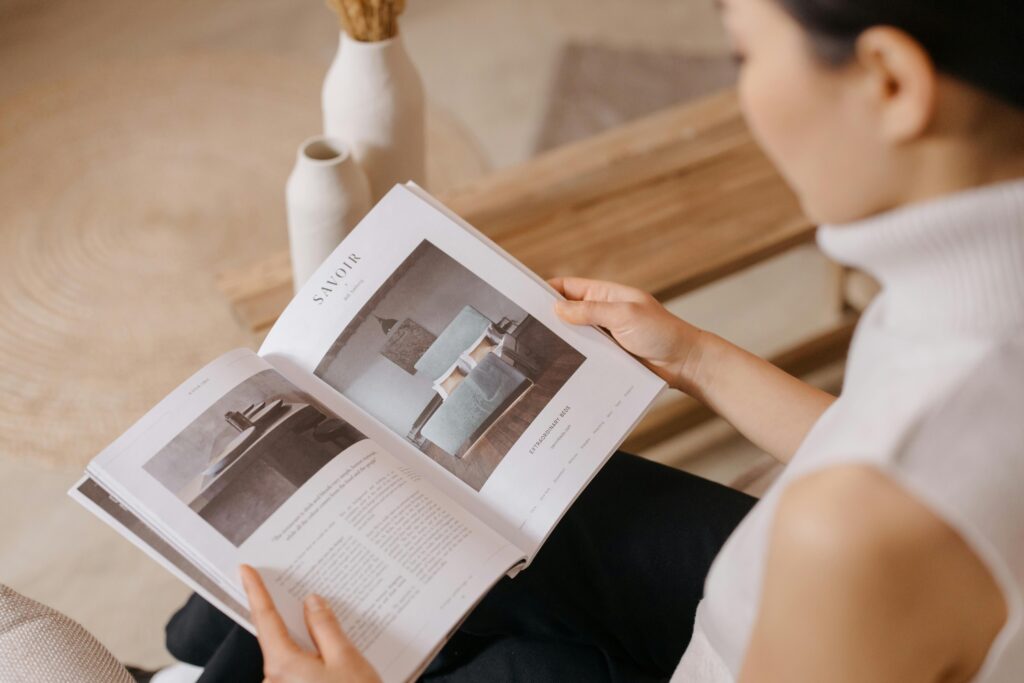 A woman in a sleeveless turtleneck reads a magazine indoors.